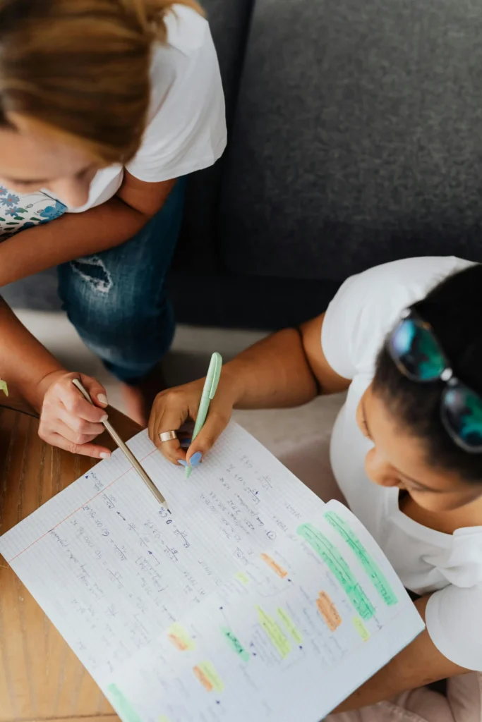 Deux personnes travaillant ensemble sur un cahier, illustrant l'accompagnement d'un jeune personnalisé dans l'apprentissage.
