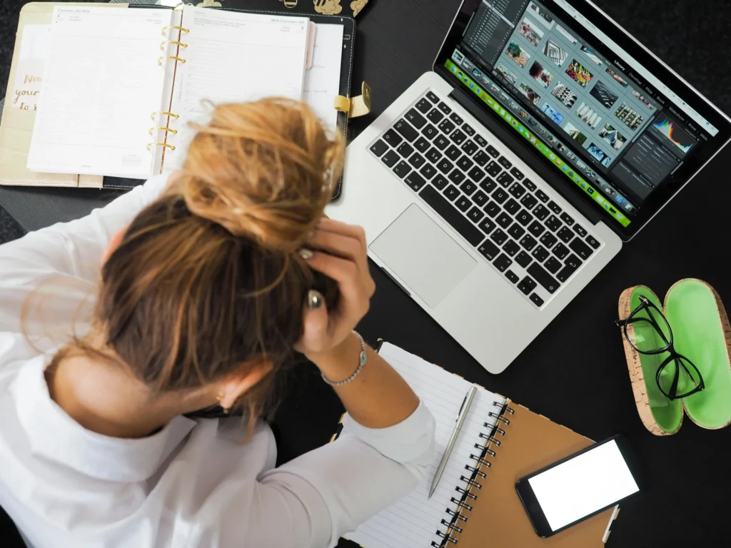 Personne se tenant la tête en regardant son bureau, illustrant le stress ou la surcharge de travail dans un contexte professionnel.